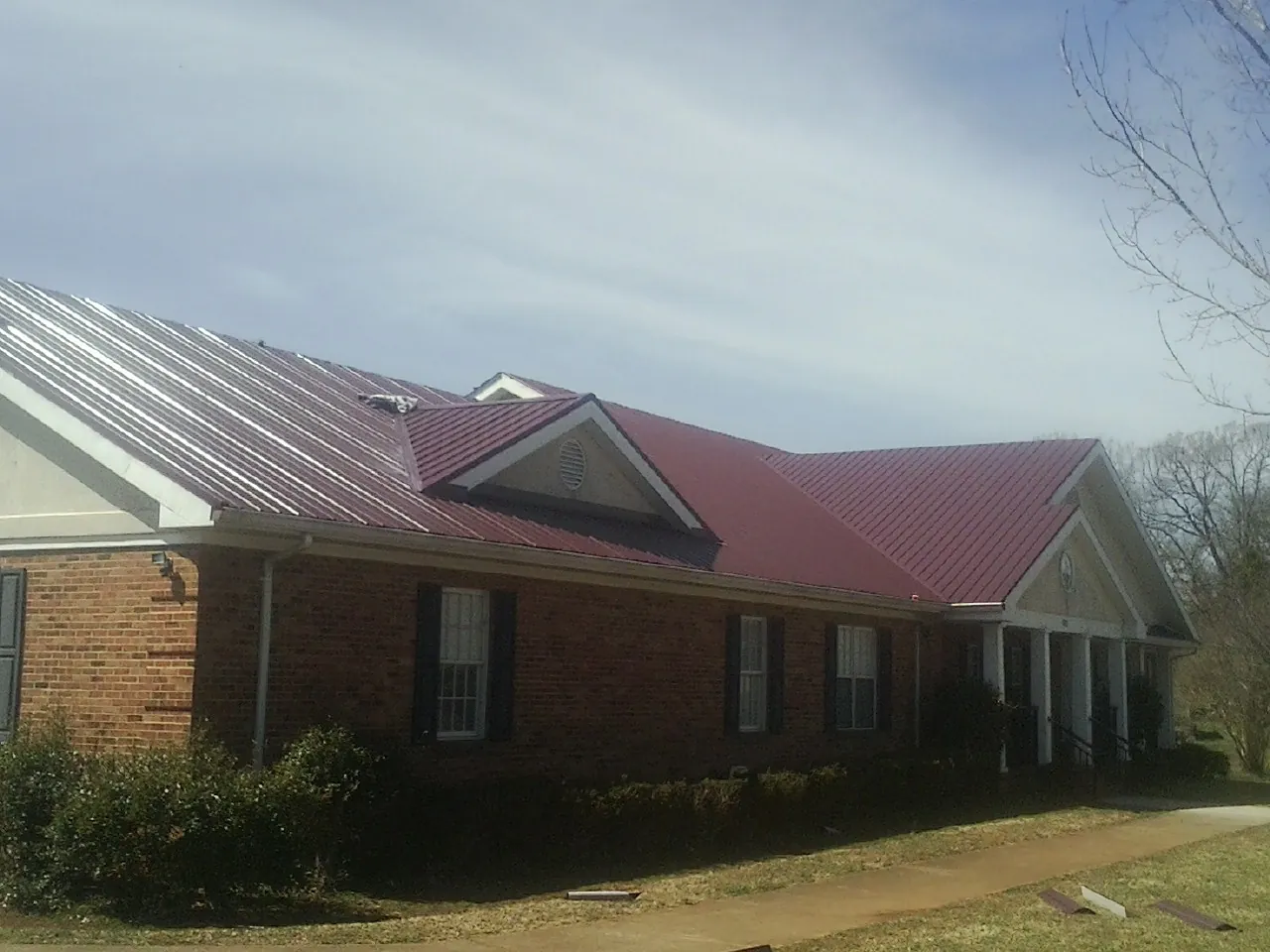 Red metal roof with gabled entries on a long brick building, from a Hail Damage Roof Repair job in Franklin
